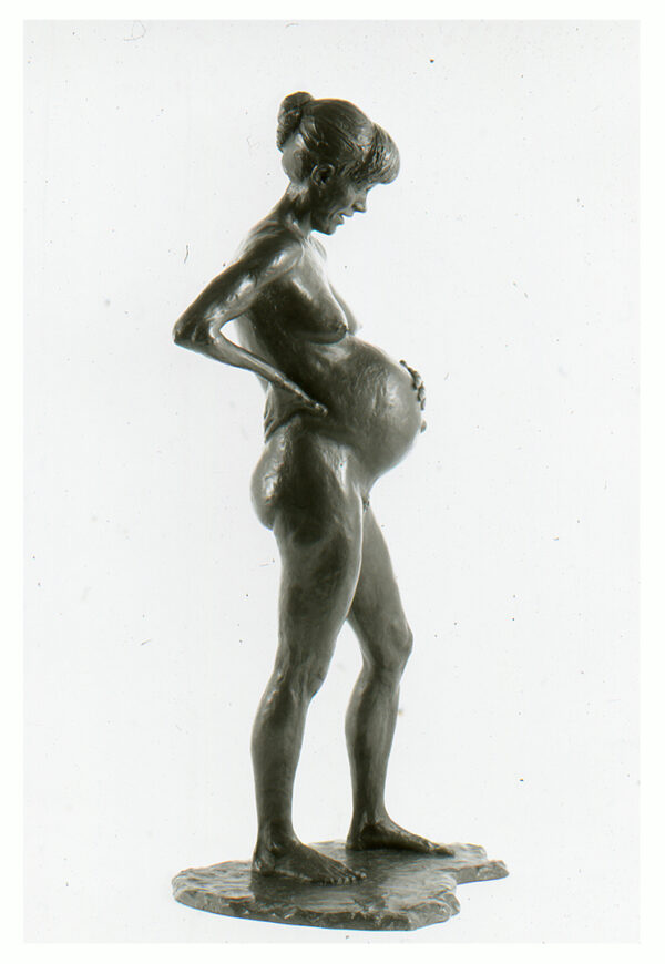 Realistic bronze sculpture table-size of a standing pregnant woman her right hand on her hip and her left hand on her belly her hair in a bun looking down.