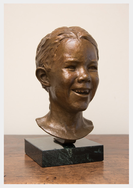 Realistic bronze sculpture of a girl with a snaggle toothed smile, hair in a braid