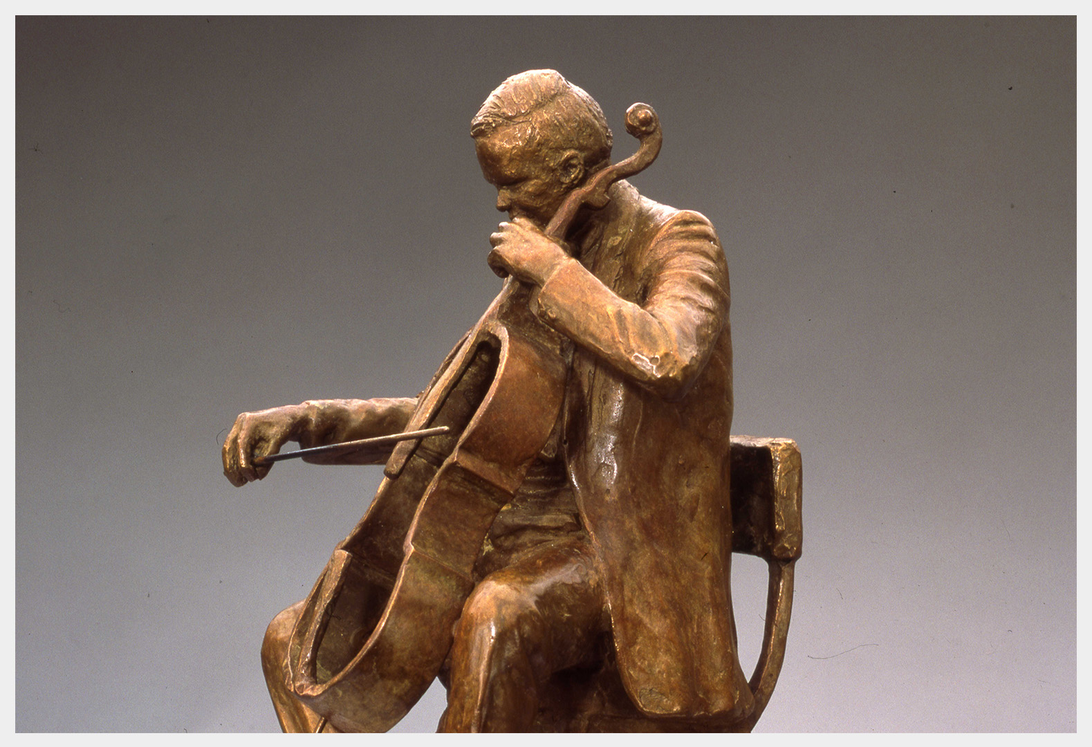 Realistic bronze sculpture life-size of a cellist sitting on a chair playing the outline of a cello with a bow