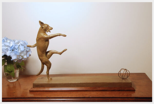 Realistic bronze sculpture on a base of a dog balanced on her right hind leg kicking a ball with her left hind foot front legs helping her balance looking forward mouth open tongue lolling out to right
