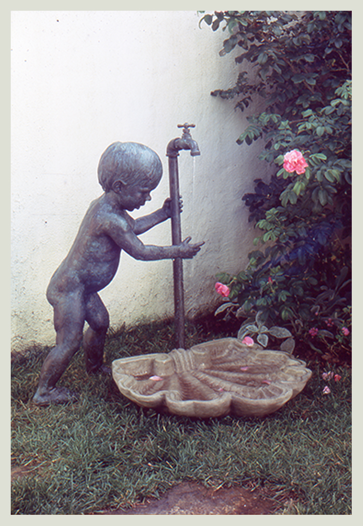 Realistic bronze sculpture of a toddler grasping water dripping from a faucet dripping into a concrete shell life-size