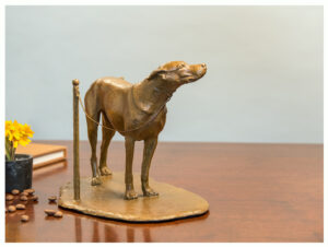 Realistic bronze sculpture table size of a dog tied to a pole waiting expectantly