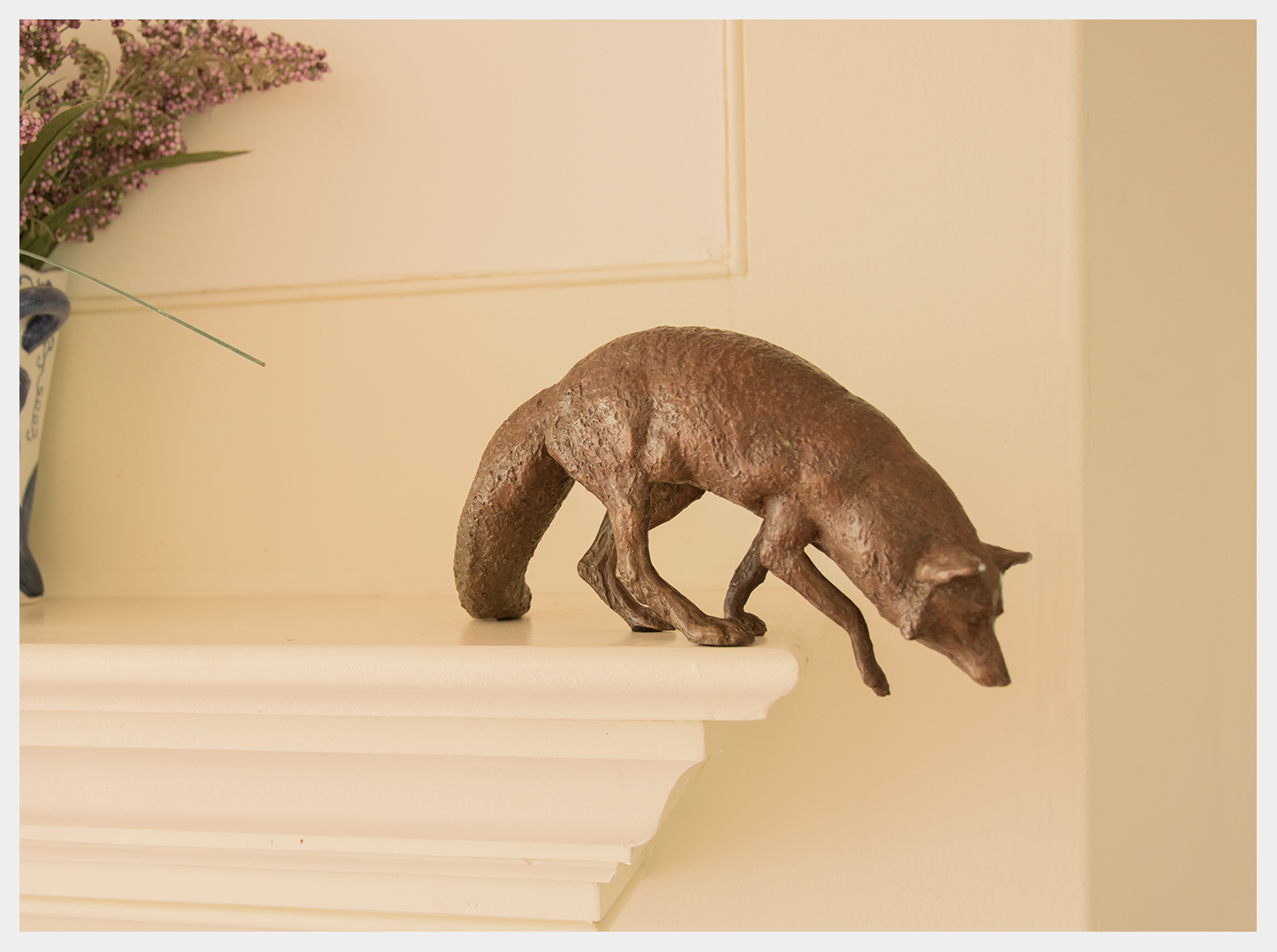 Realistic mantel-piece sized bronze sculpture of a fox starting to jump off a structure.