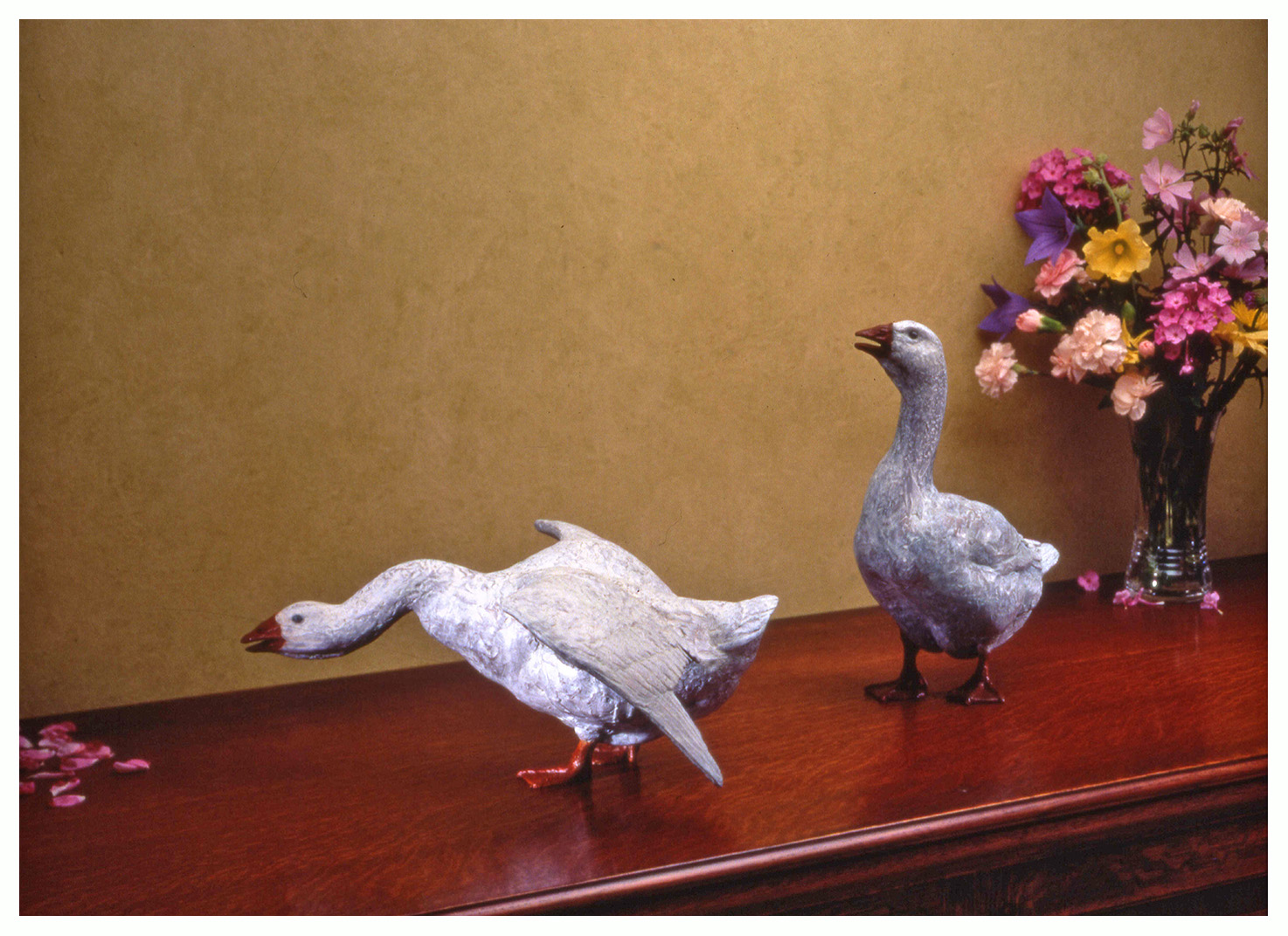 Realistic bronze sculpture of two table size geese, both honking one alert with its head up and wings folded the other aggressive with wings spread and neck extended